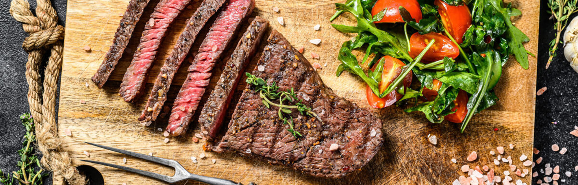 Medium-rare rump steak on a chopping board with cherry tomatoes and leafy salad