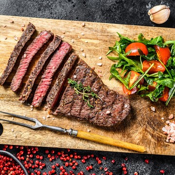 Medium-rare rump steak on a chopping board with cherry tomatoes and leafy salad